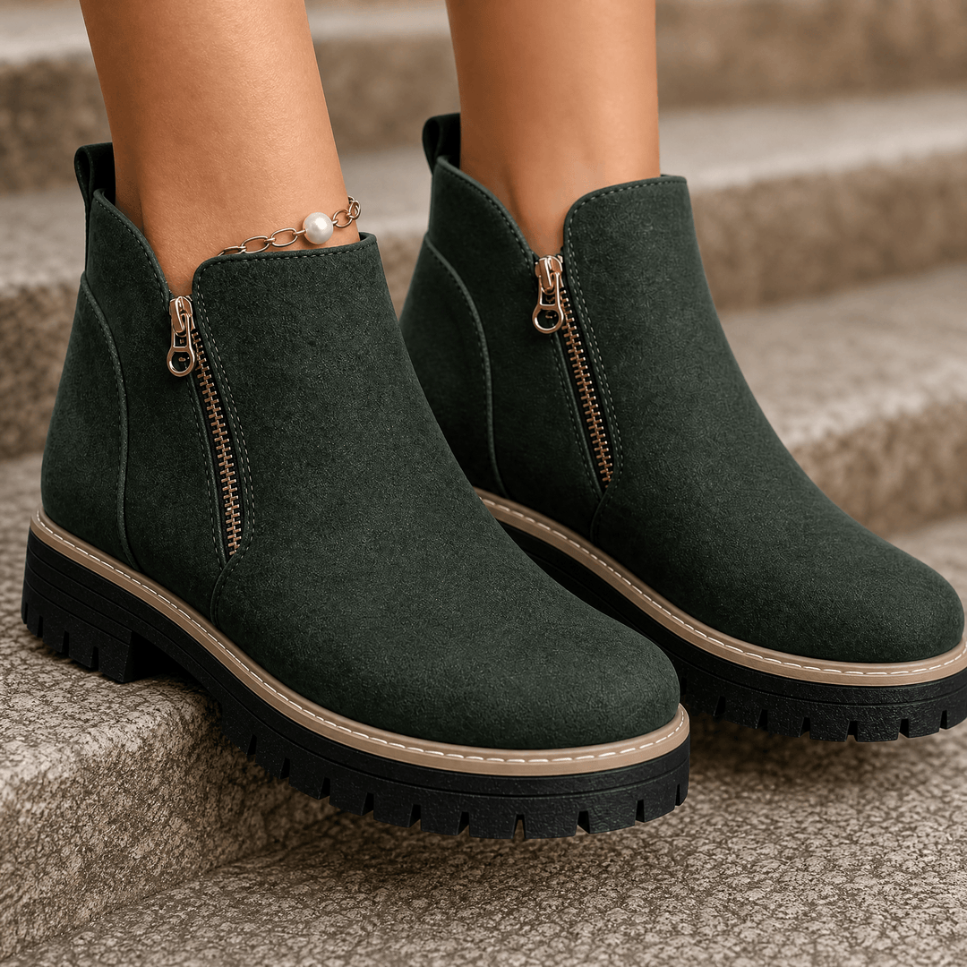 Dark green suede platform ankle boots with gold side zips and lug soles, worn on stone steps