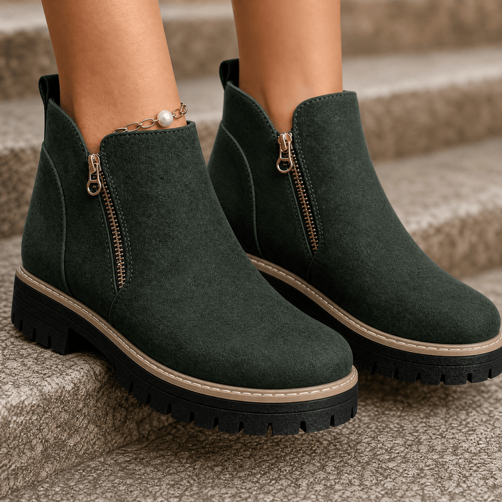 Dark green suede platform ankle boots with gold side zips and lug soles, worn on stone steps