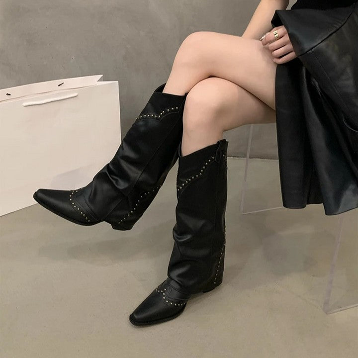 Black studded slouch knee boots with a pointed toe, seated view