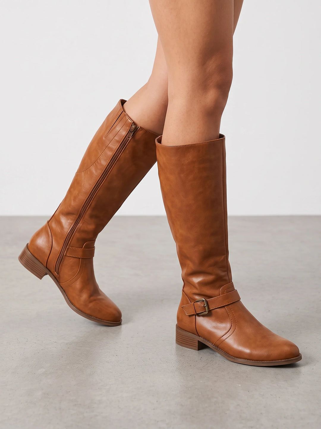 Tan leather riding boots with a buckled ankle strap, side view