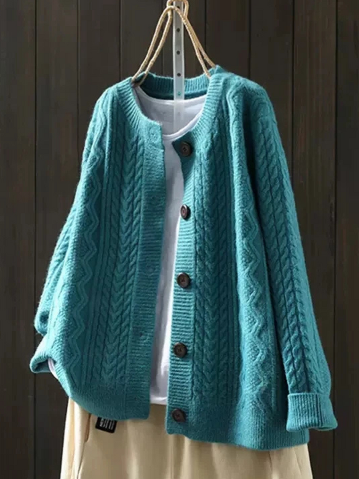 Teal cable knit cardigan on a hanger with brown buttons, styled over a white top and cream skirt