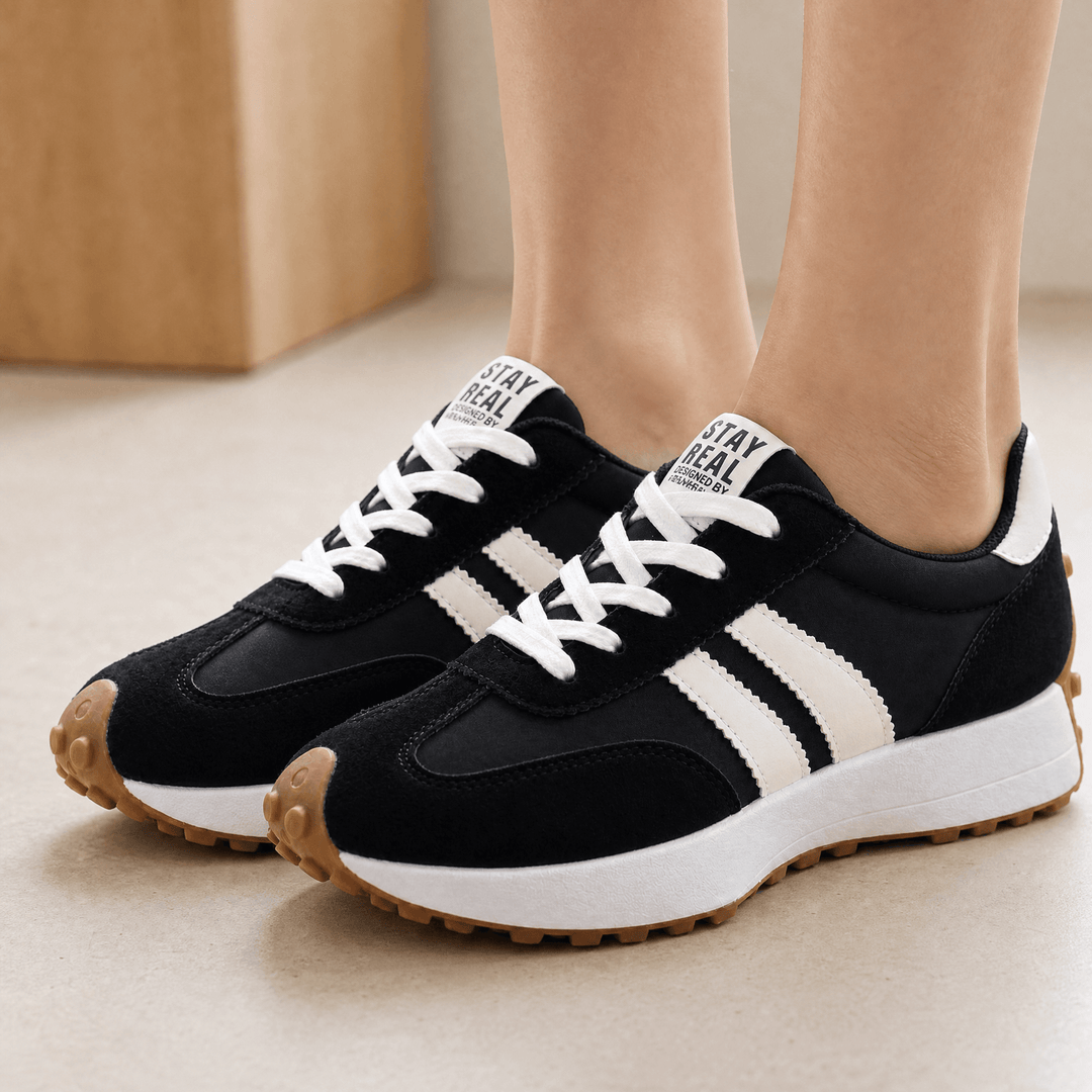 Black suede sneakers with cream side stripes, white laces and gum soles, worn indoors