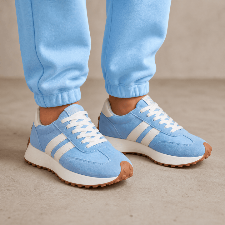 Light blue suede sneakers with white side stripes and gum soles, worn