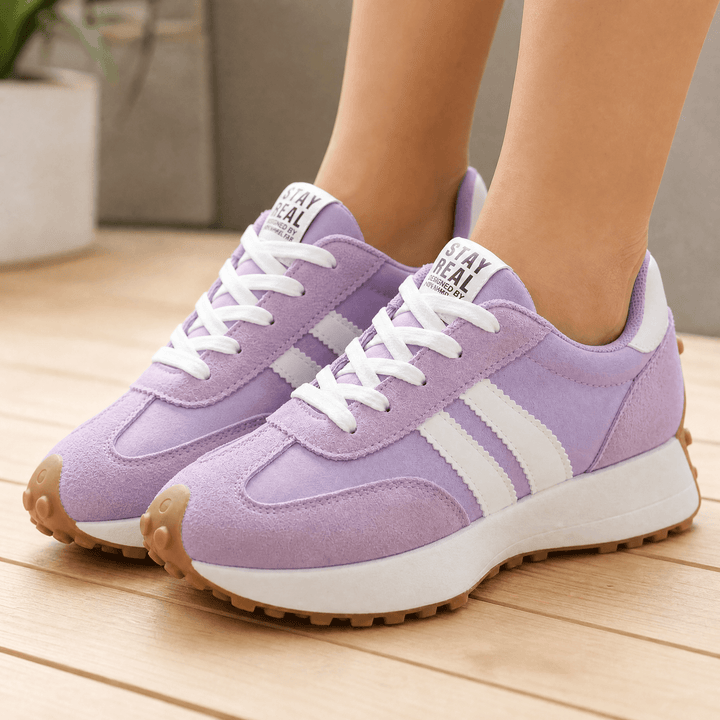 Pair of lilac suede sneakers with white side stripes and gum soles, worn