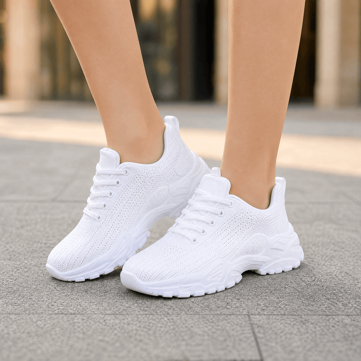 All white knit sneakers with chunky textured soles worn on a sidewalk