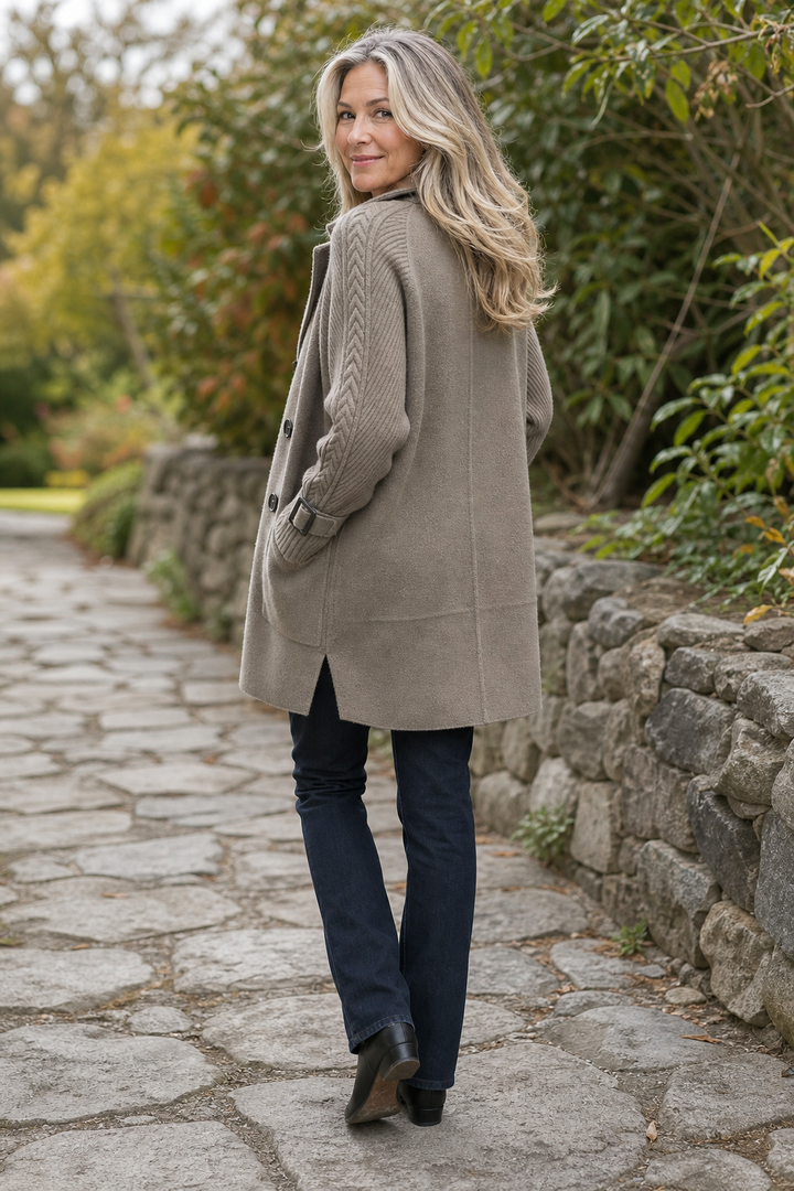 Back view of a taupe coat with cable knit sleeves on a path