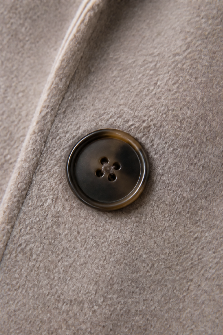 Close up of a horn button on a taupe wool blend coat
