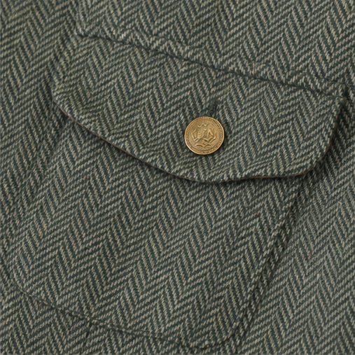 Brass button and flap pocket detail on an olive herringbone jacket