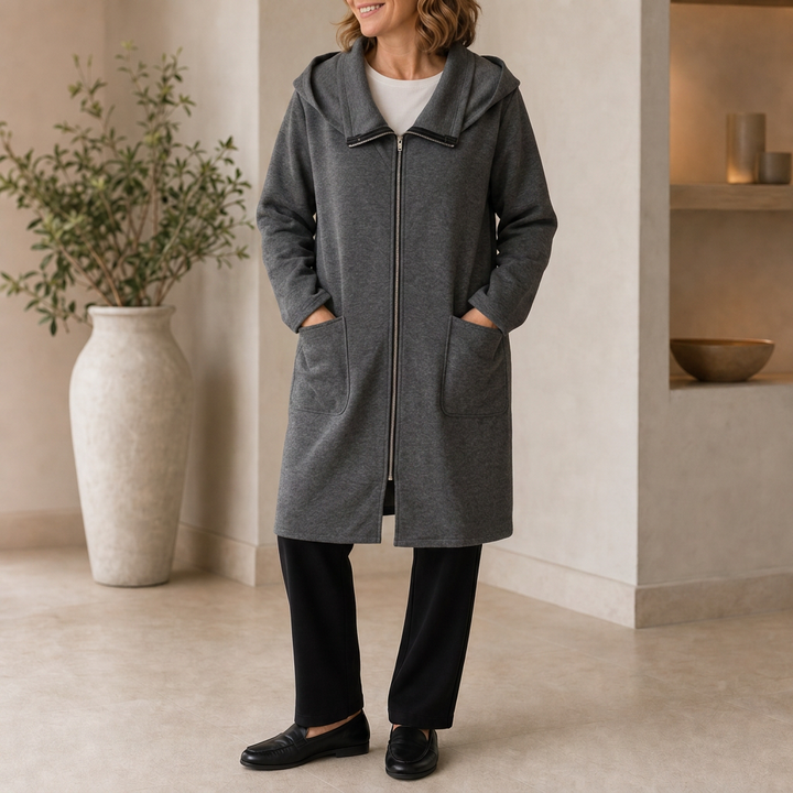 Grey hooded travel coat worn with black trousers indoors