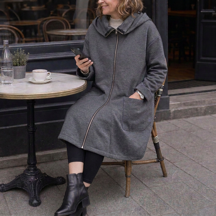 Woman seated at a cafe table in a grey hooded travel coat