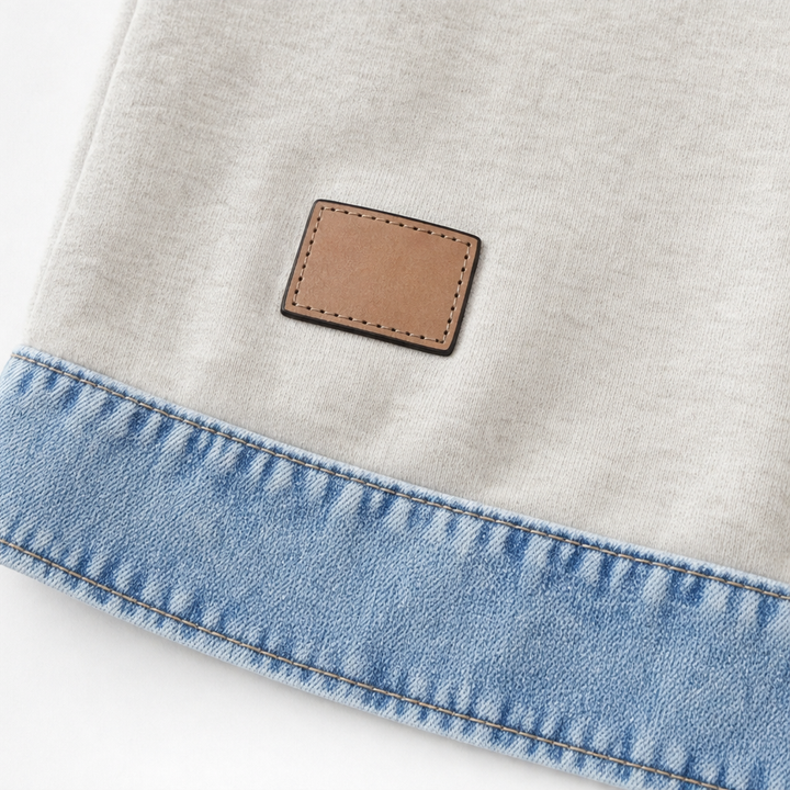 Leather patch above the denim hem band on a cream sweatshirt