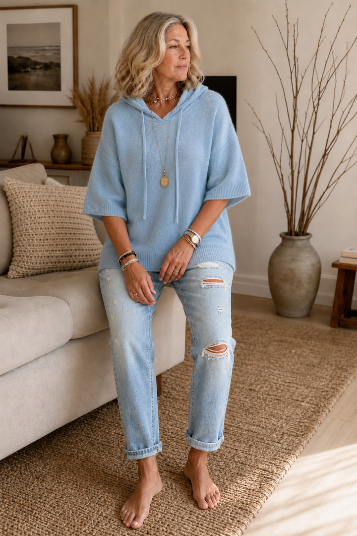 Light blue knit hoodie worn with ripped jeans in a living room
