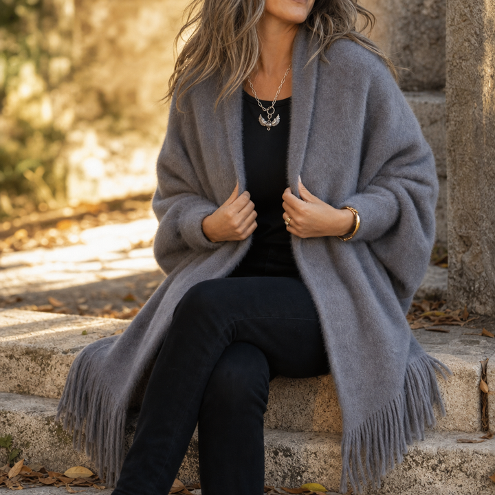 Woman seated on a wall in a grey draped fringed shawl wrap