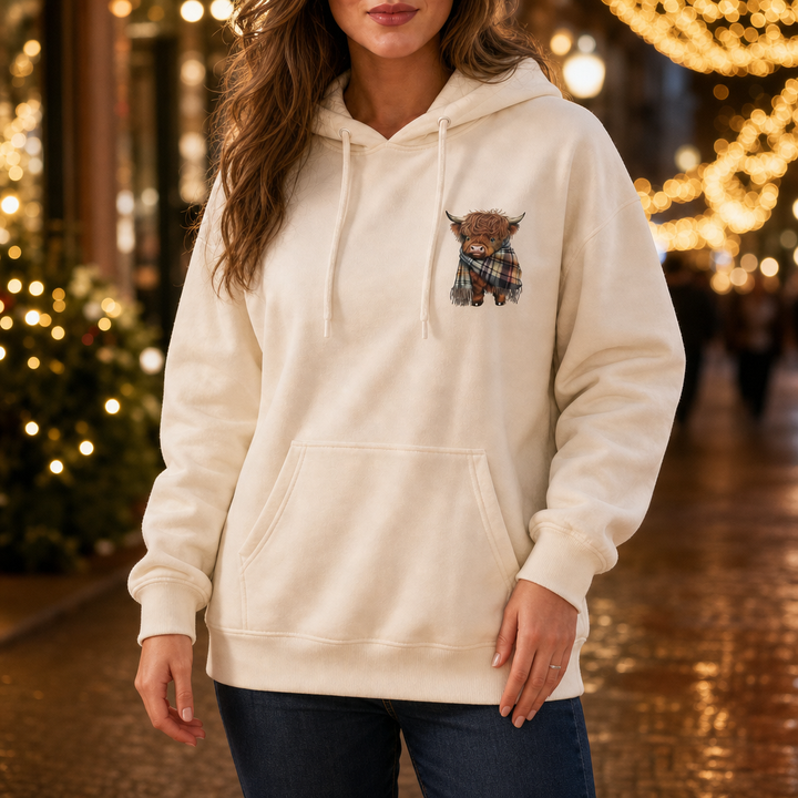Cream highland cow hoodie worn on a street with festive lights