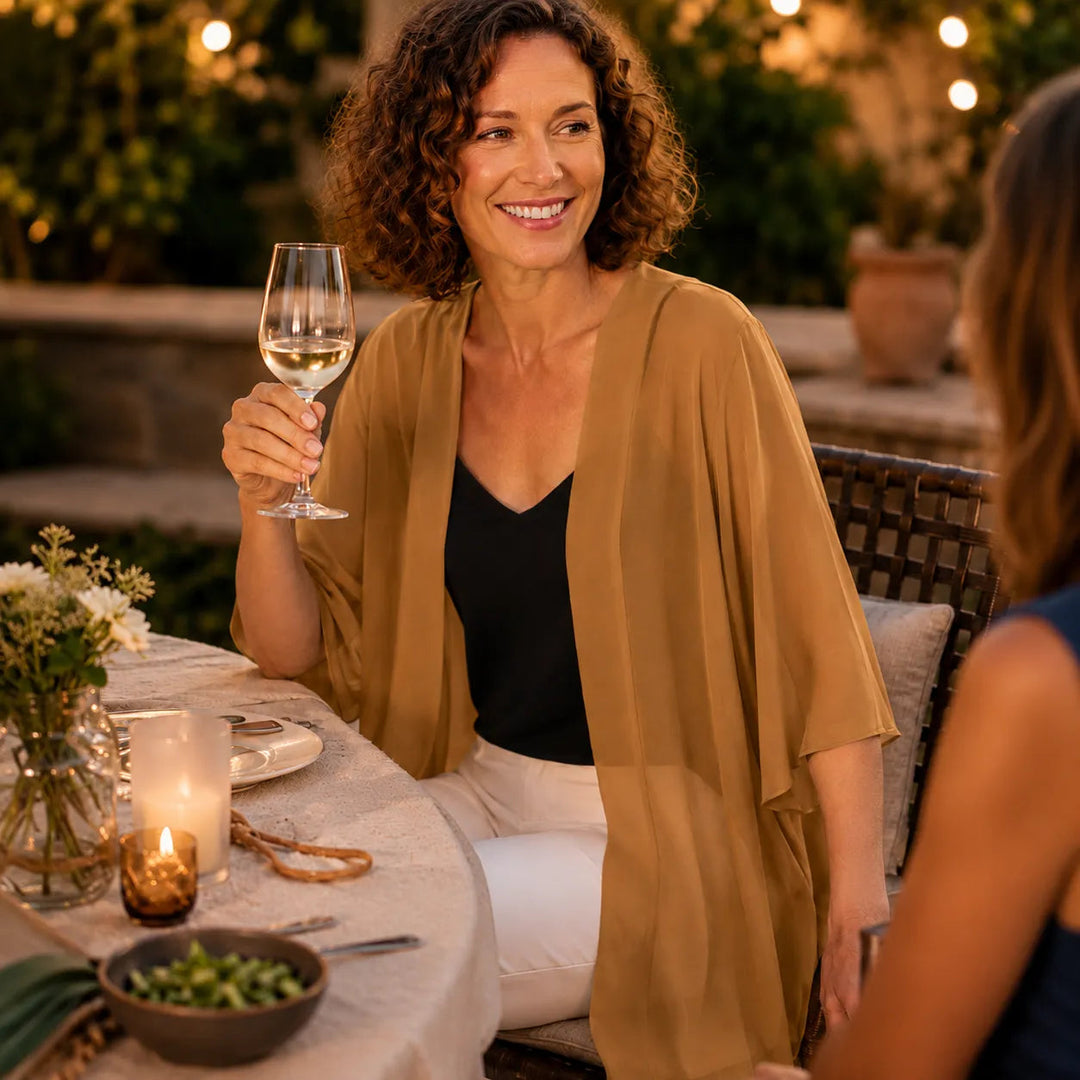 Woman with a wine glass at an evening table in a camel cardigan
