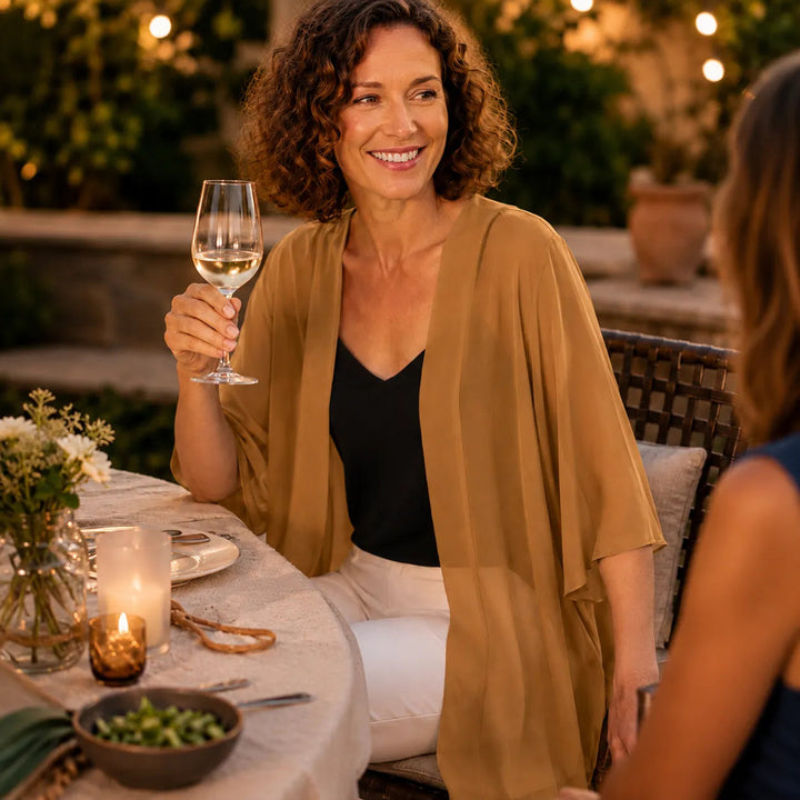 Woman with a wine glass at an evening table in a camel cardigan