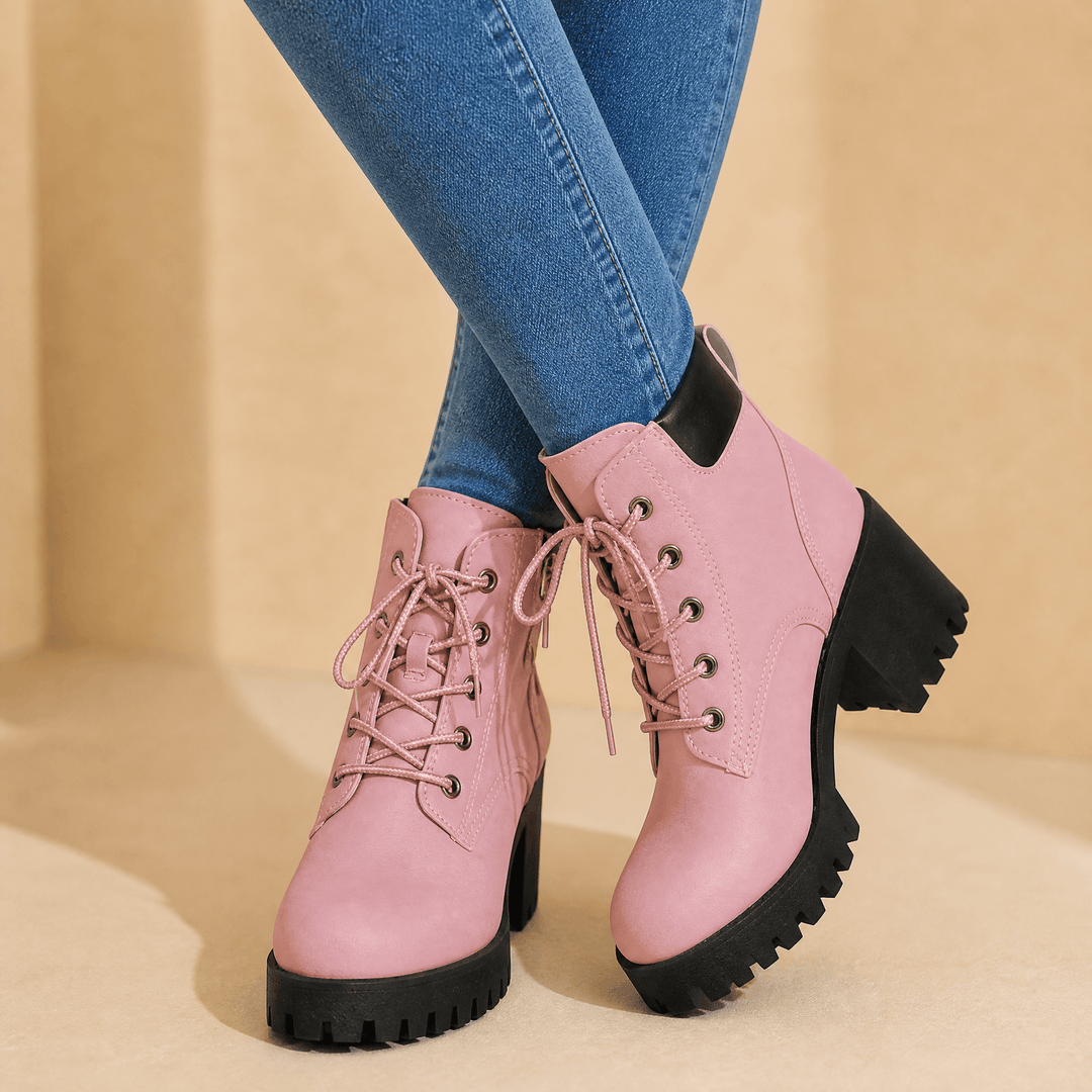 Pink lace-up platform combat boots worn with blue jeans against a beige backdrop