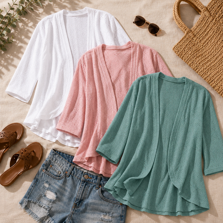 Flat lay of white, pink and sage eyelet cardigans with a straw bag