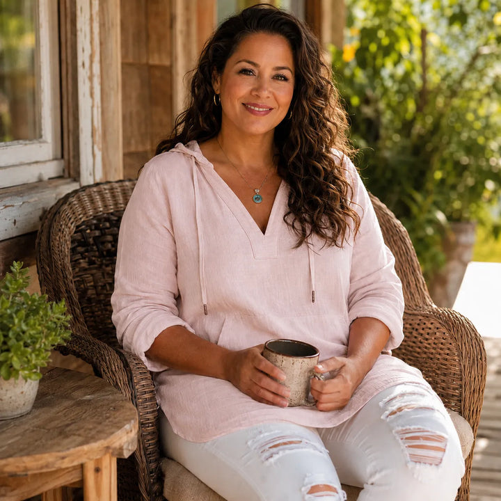 Woman seated outdoors in a blush pink V neck hooded top