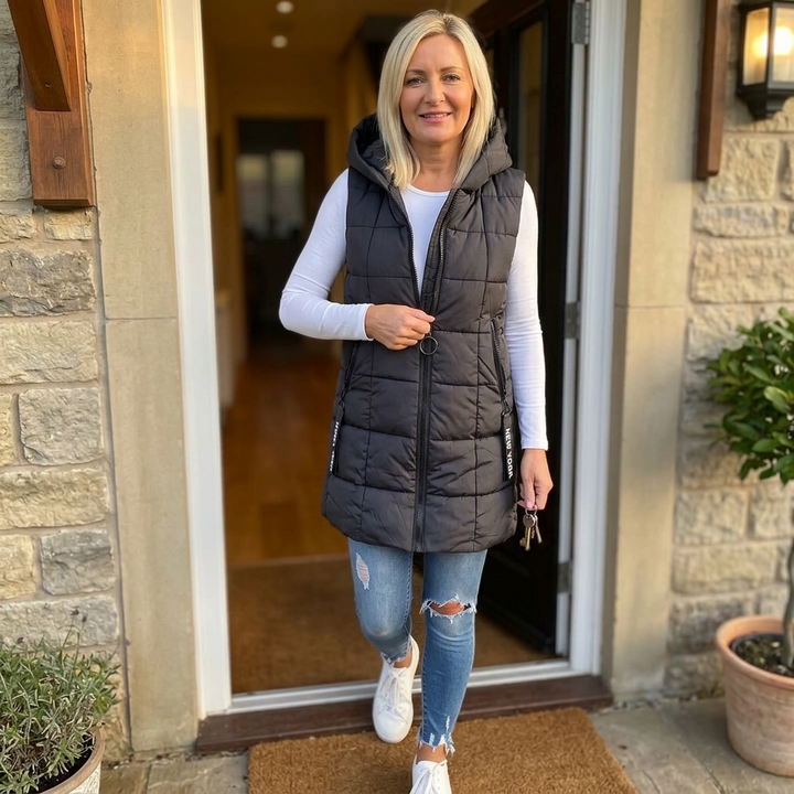 Black long quilted puffer vest worn in a doorway with jeans