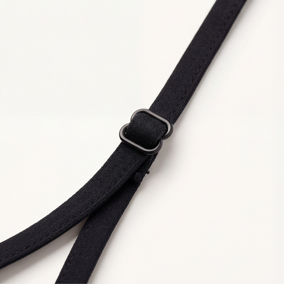 Thin black bra strap with its slider on a white surface