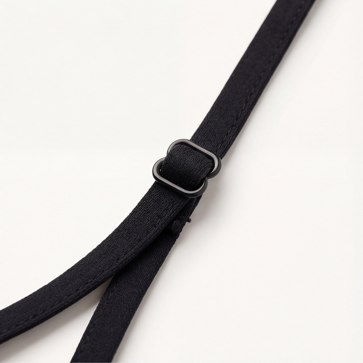 Thin black bra strap with its slider on a white surface