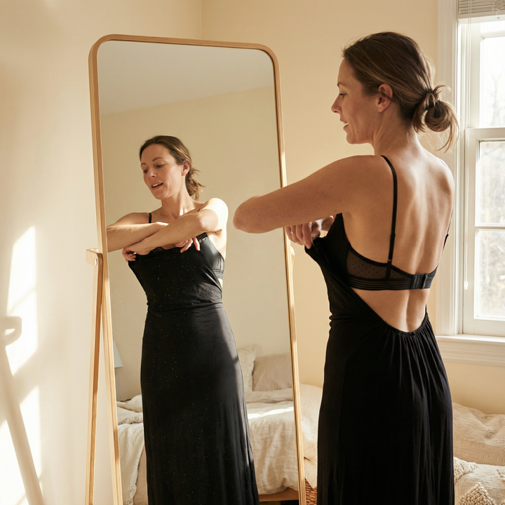 Woman at a mirror fastening a black low-back dress