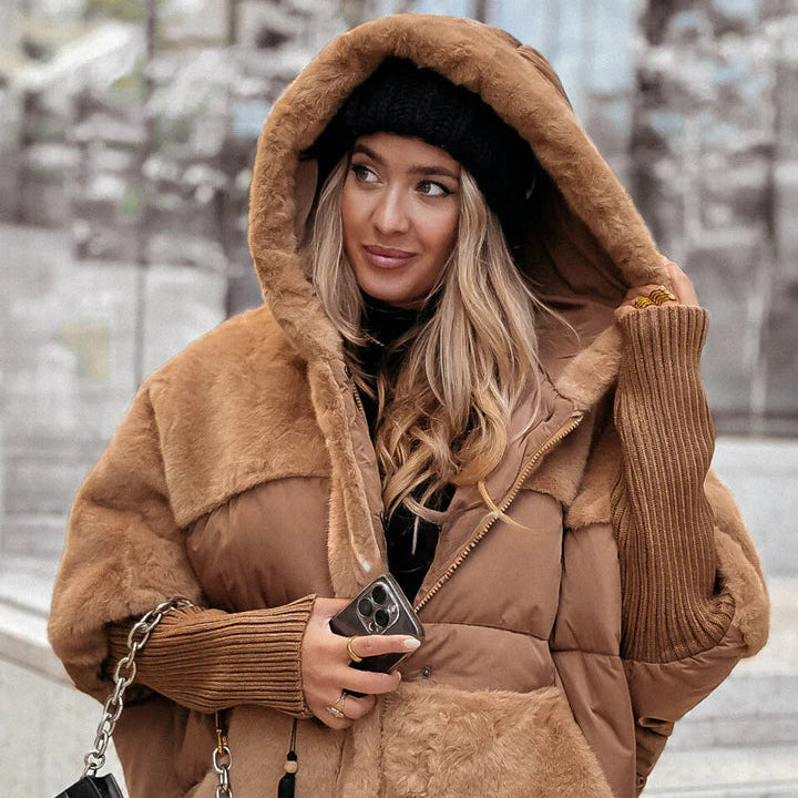 Woman holding up the fur lined hood of a camel quilted jacket