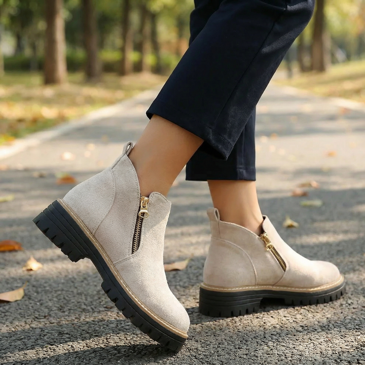 Cream suede chelsea boots worn with navy trousers outdoors
