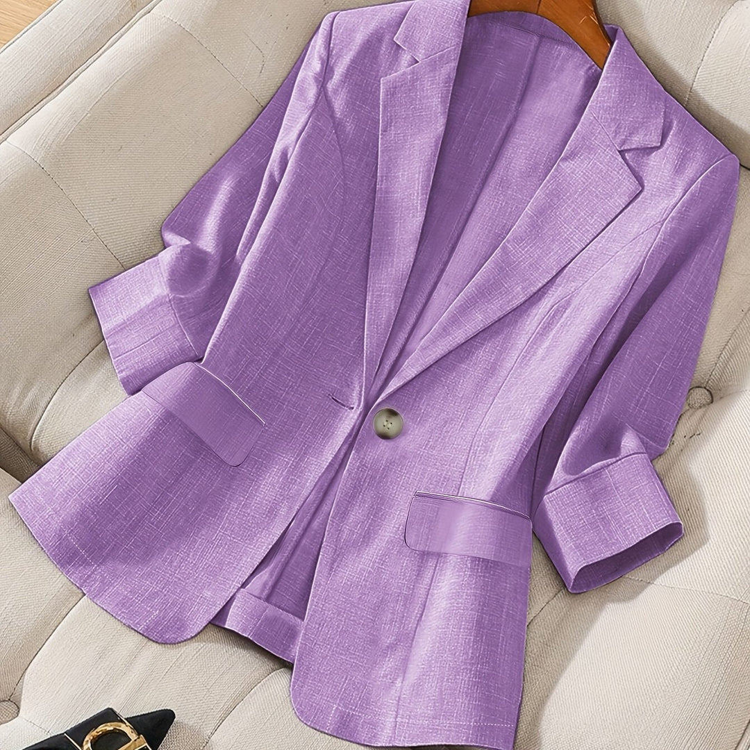 Lilac cropped blazer with rolled cuffs laid on a cream sofa