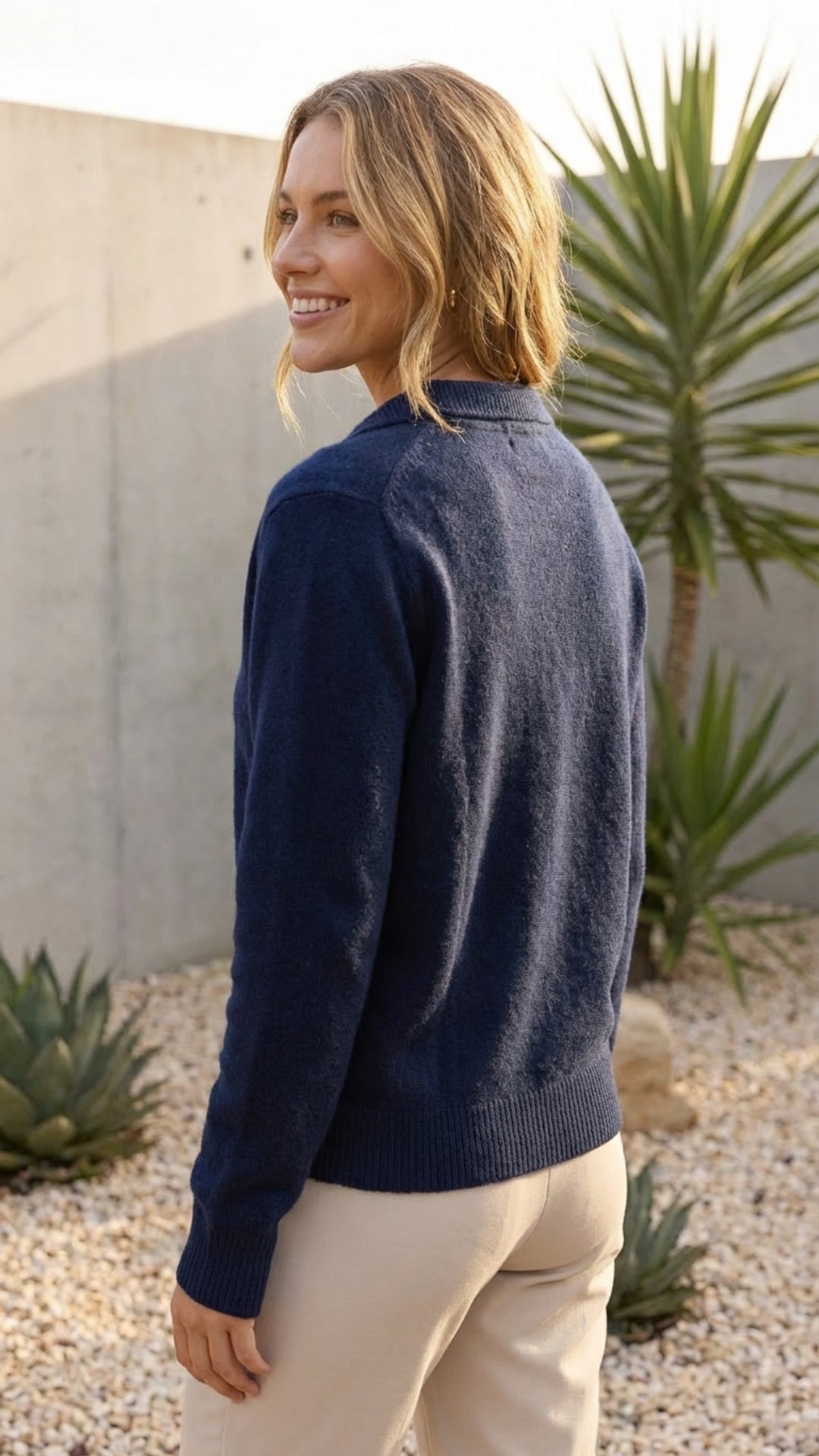 Navy collared knit cardigan worn with cream trousers outdoors, back view