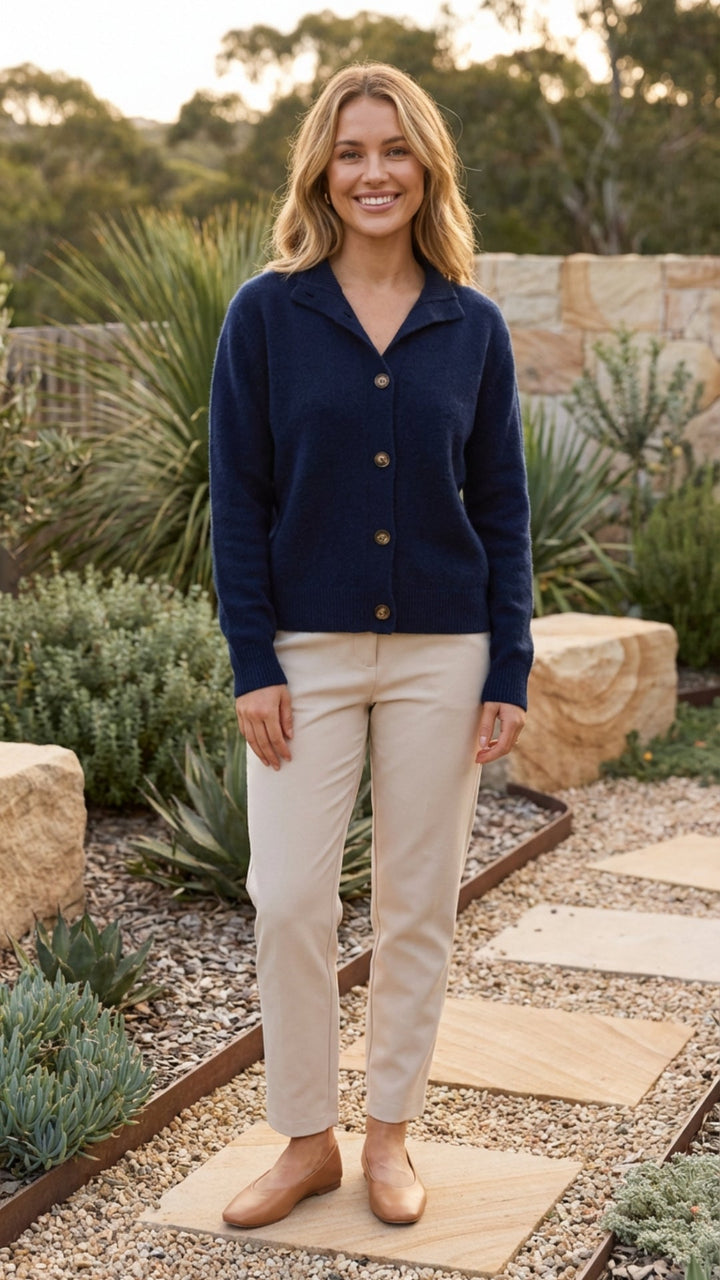 Navy collared button front knit cardigan worn with cream trousers in a garden, full length front view