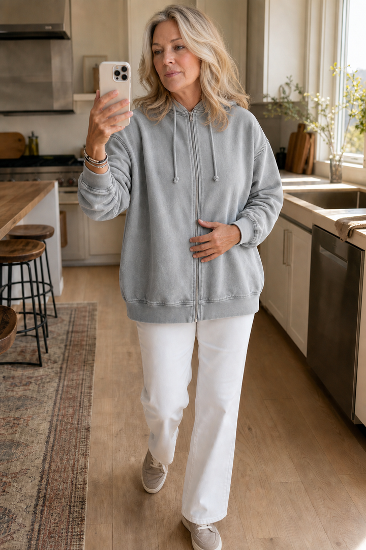 Grey washed zip up hoodie worn in a kitchen with white jeans