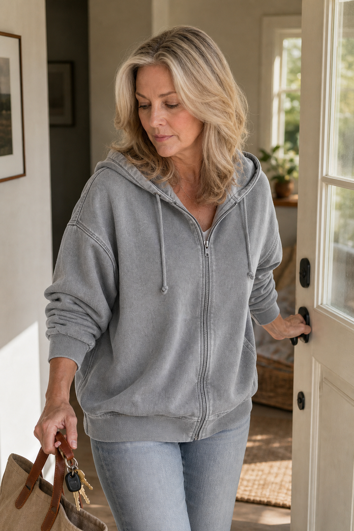Grey washed zip up hoodie worn in a doorway with jeans